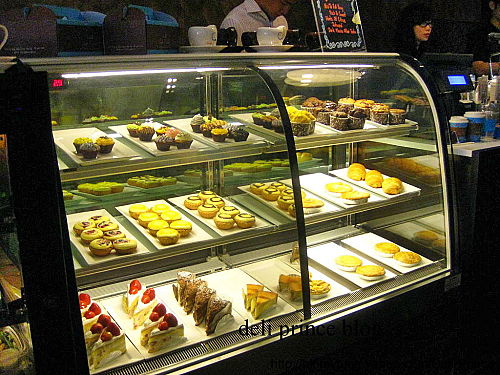 Cup cake, pastry and cheesecake are displayed in the fridge.